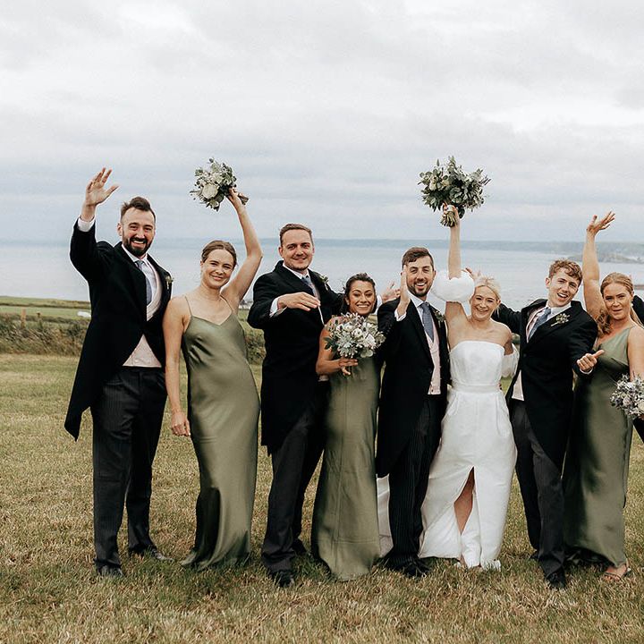 Bride & groom stand with groomsmen in morning suits and bridesmaids in green satin bridesmaid dresses 