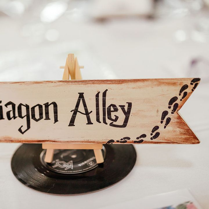 Quirky wedding table number sign in the style of Harry Potter; cream arrow sign with "Diagon Alley" lettering in the Harry Potter font