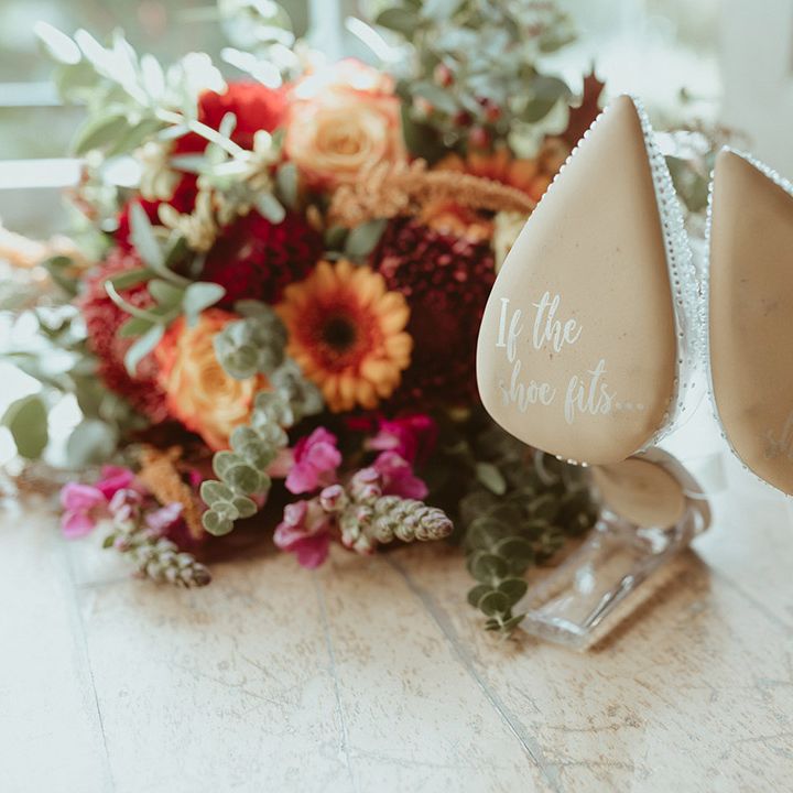 Plastic Cinderella wedding shoes with sparkles and writing on the sole of the shoe with autumnal wedding bouquet 