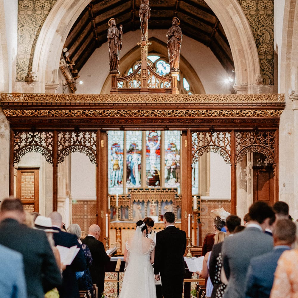The bride and from stand at the altar for the church wedding ceremony with pastel coloured wildflowers decorating the aisle 
