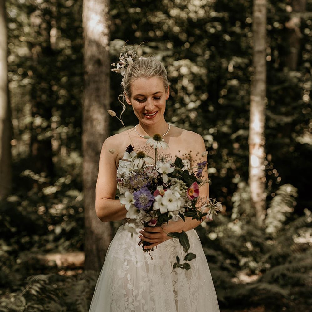 Bride in strapless Milla Nova wedding dress with purple and white wedding bouquet made up of wildflowers 