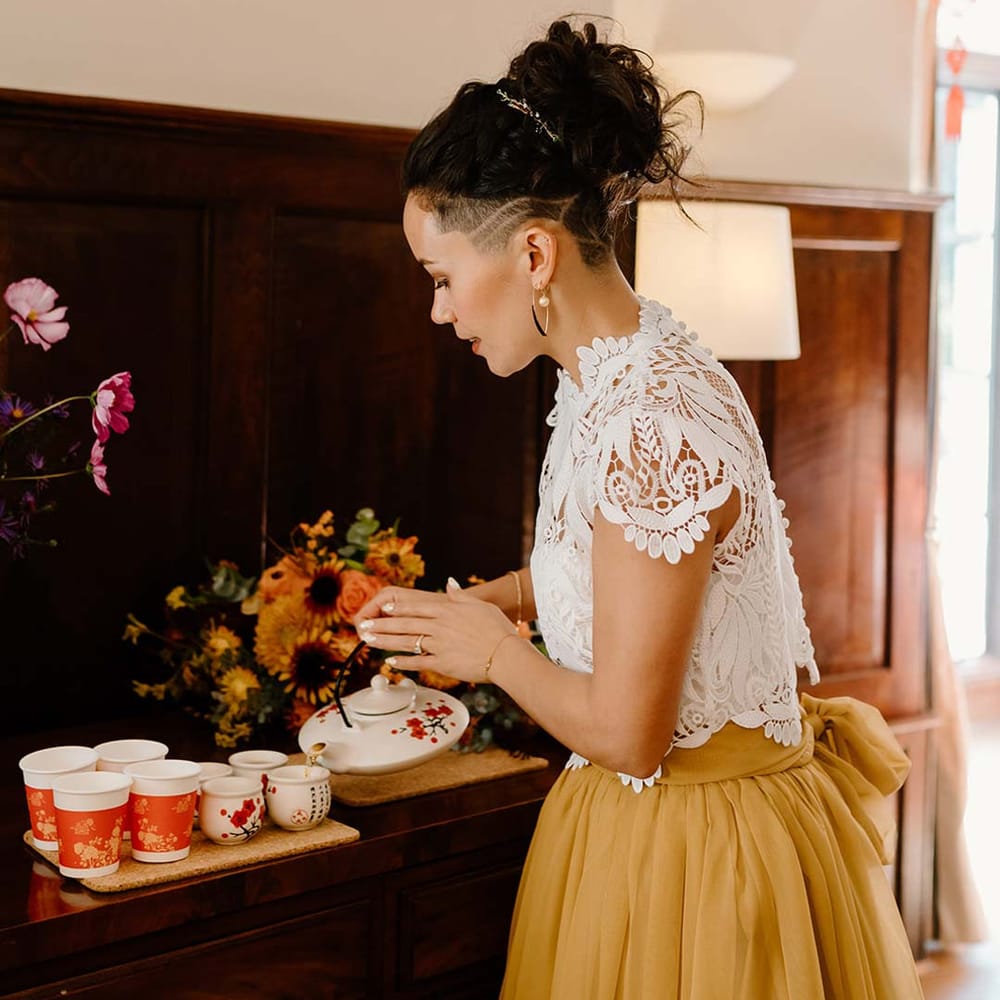 Bride in white mesh lace bridal crop top and yellow wedding skirt partaking in Chinese Tea Ceremony at Broadfield Court