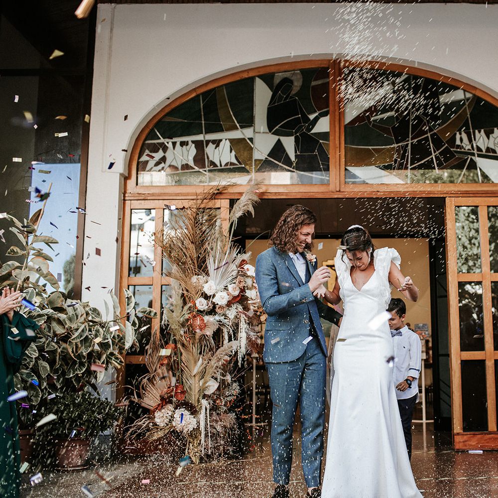 Confetti moment with bride in a ruffle sleeve Rime Arodaky wedding dress and groom in a navy blue three-piece suit