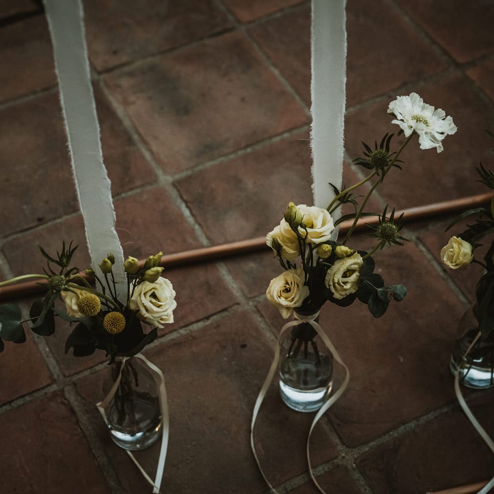 Wedding flowers in glass bottles weighing down the table plan pinned to ribbon