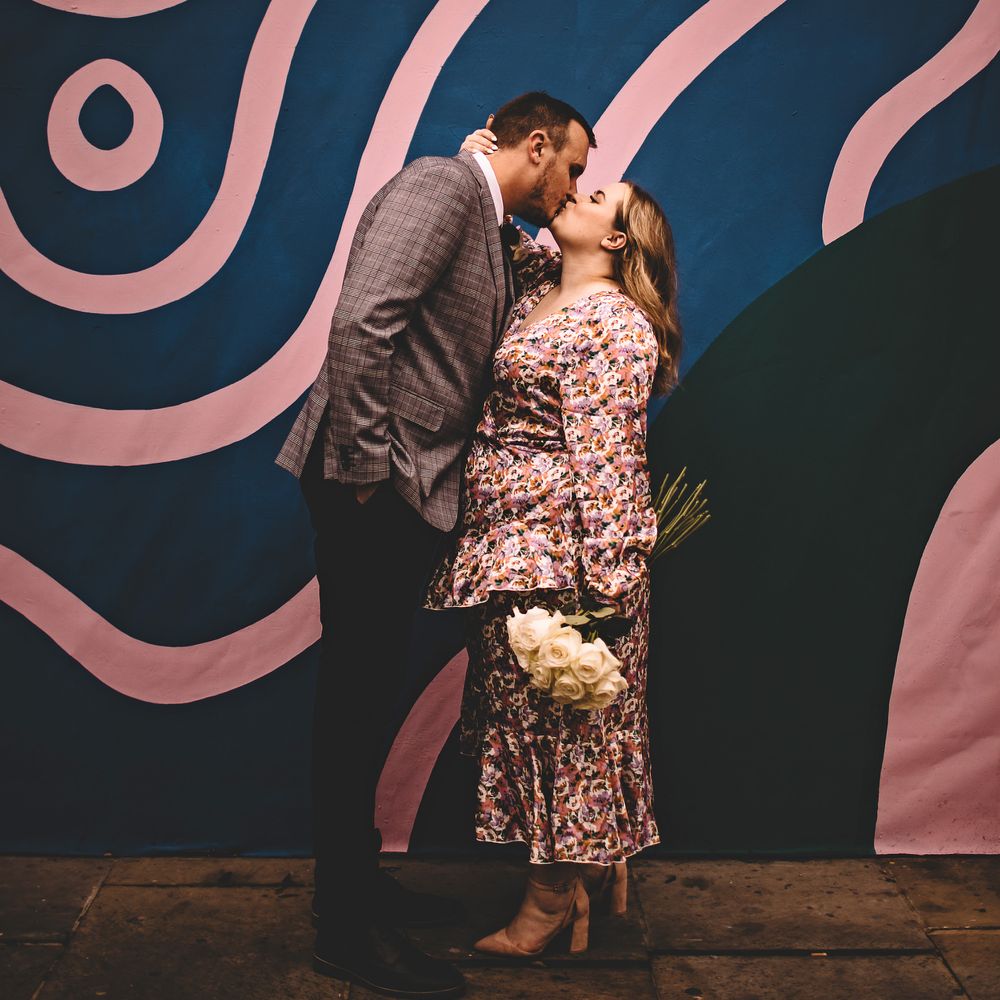 Bride & groom kiss in front of wall painted with pink and blue stripes