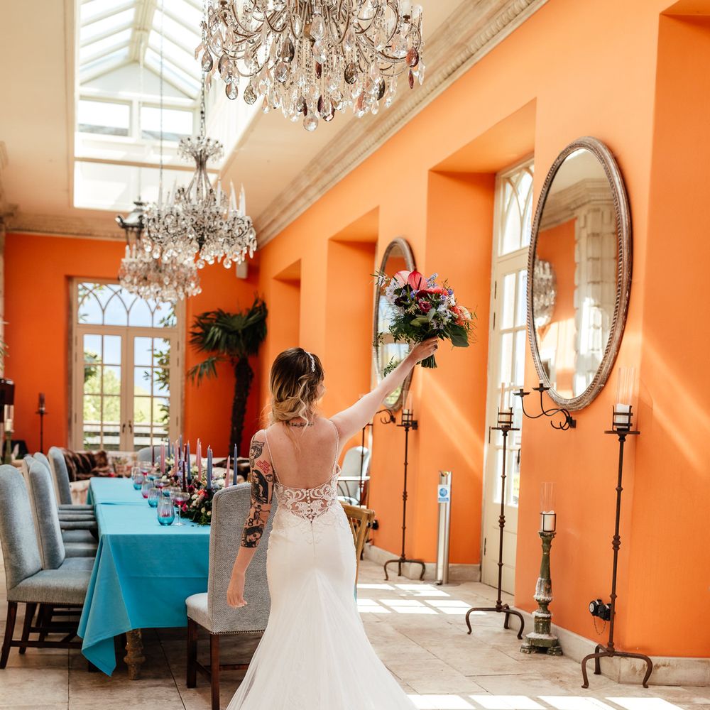 Bride holds out colourful bouquet in bright orange room