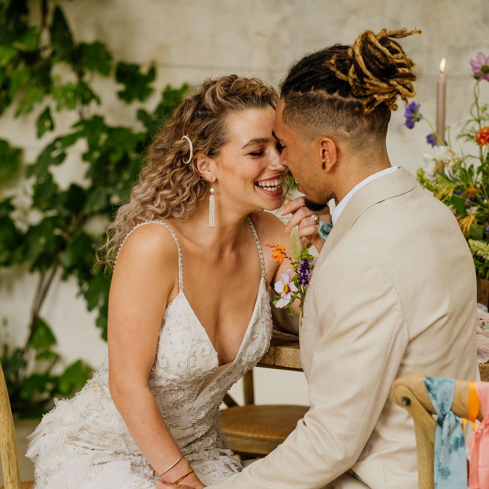 Groom in a beige suit holding hands with his curly haired bride in an embellished wedding dress