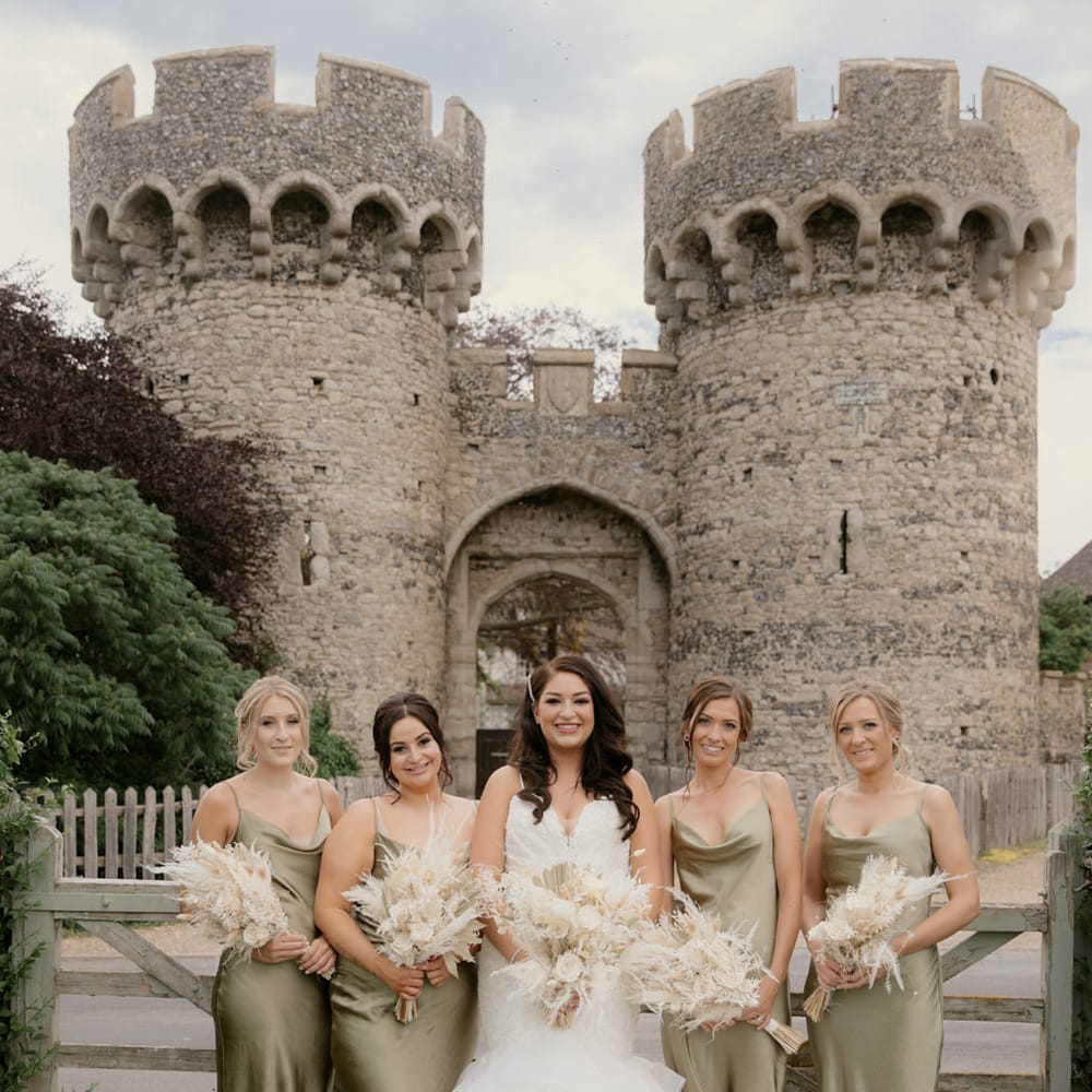 Bridal party portrait in front of Cooling Castle Barn wedding venue in green satin bridesmaid dresses and fishtail wedding dress