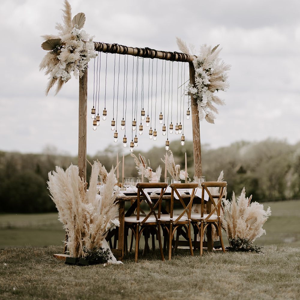 Wooden table and chairs on a hill at Waresley Park Estate decorated with pampas grass arrangements and hanging Edison bulbs