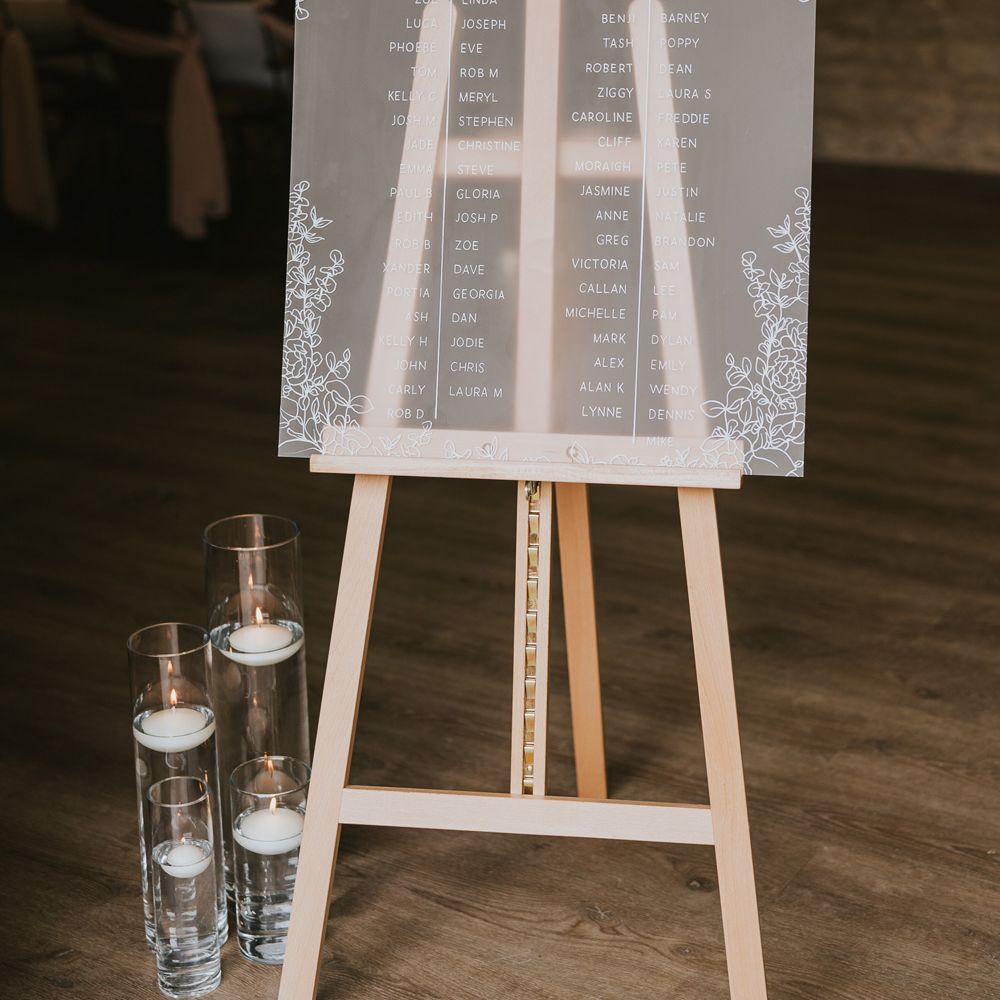 Frosted acrylic table seating plan on wooden easel with candles and white and green floral decor at Tythe Barn wedding with barn wedding flowers