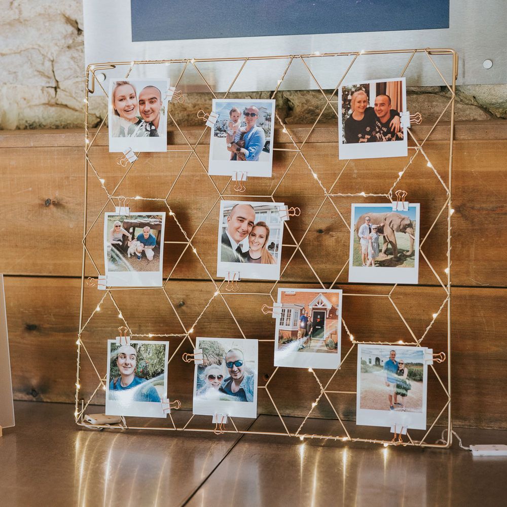 Gold wire frame with lights and polaroids next to frosted acrylic wedding sign with quote at Tythe Barn wedding with barn wedding flowers