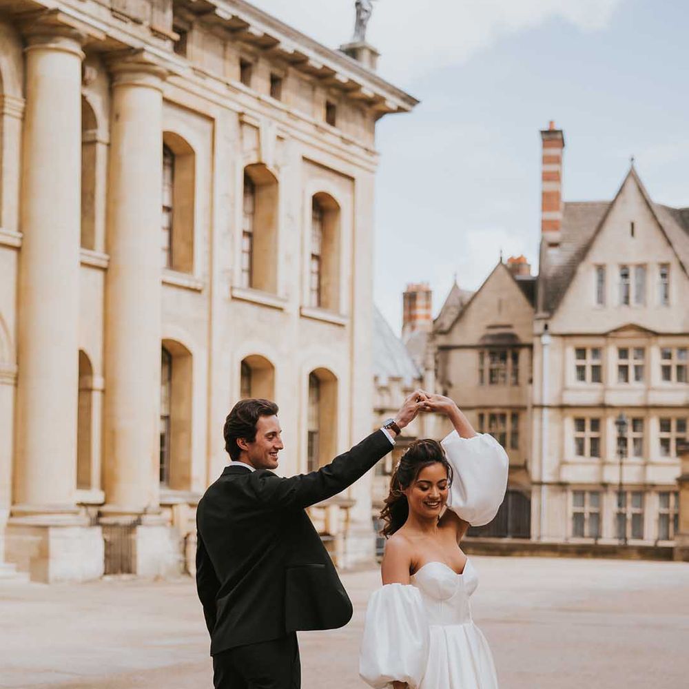 Groom in a tuxedo twirling his bride in a strapless wedding dress with detachable puff sleeves at Bodleian Library