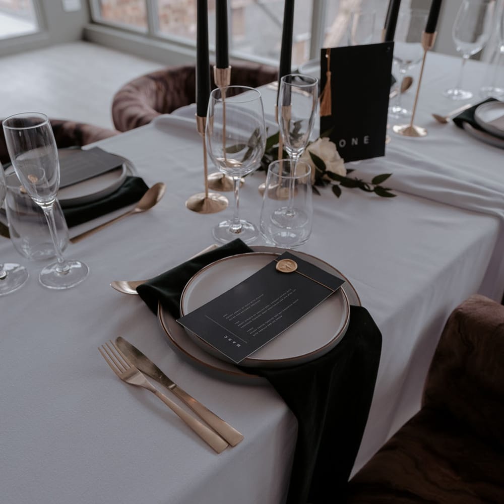 Elegant place setting with black table cloth, gold cutlery and wax seal on the menu card 