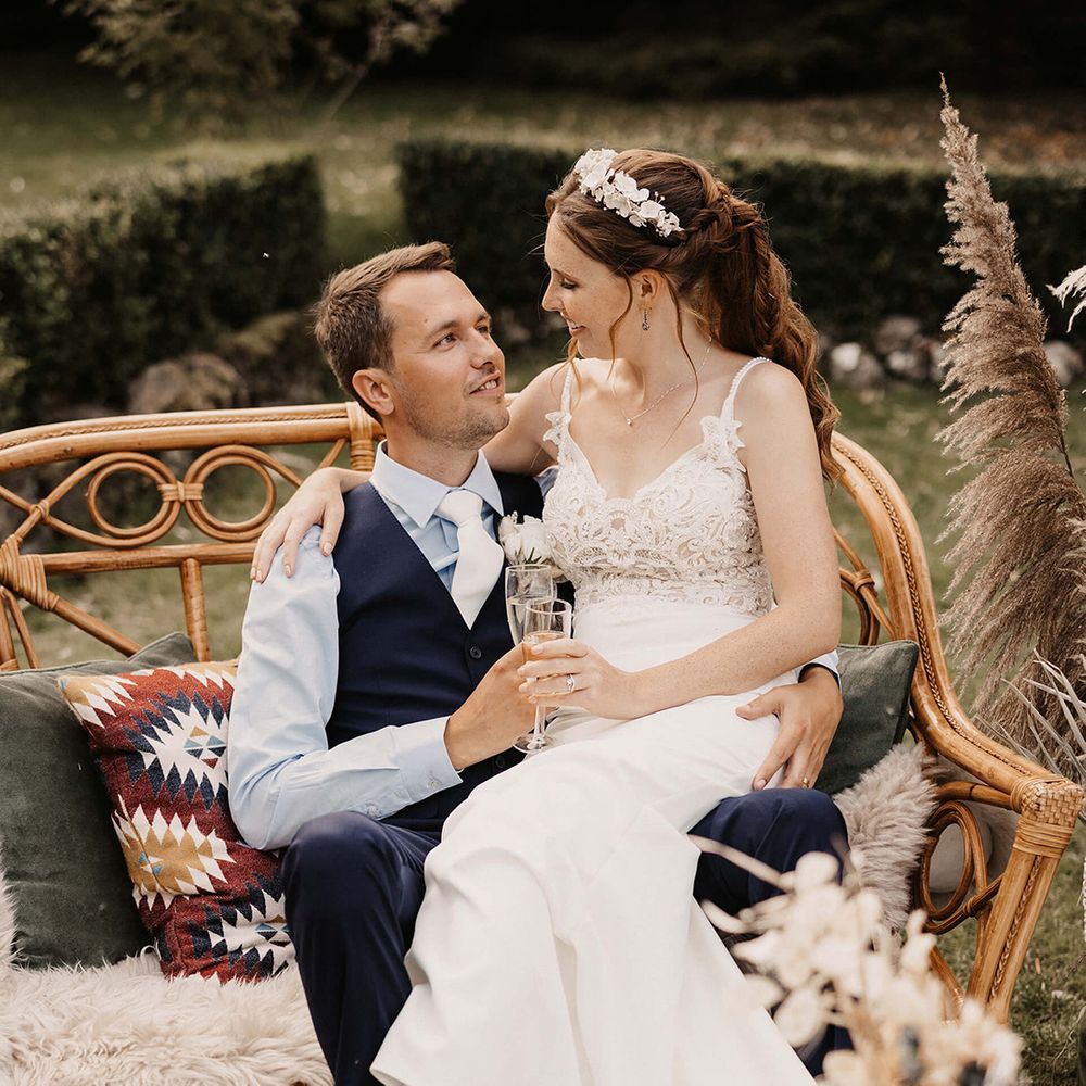 Bride sits on her grooms lap outdoors on their wedding day