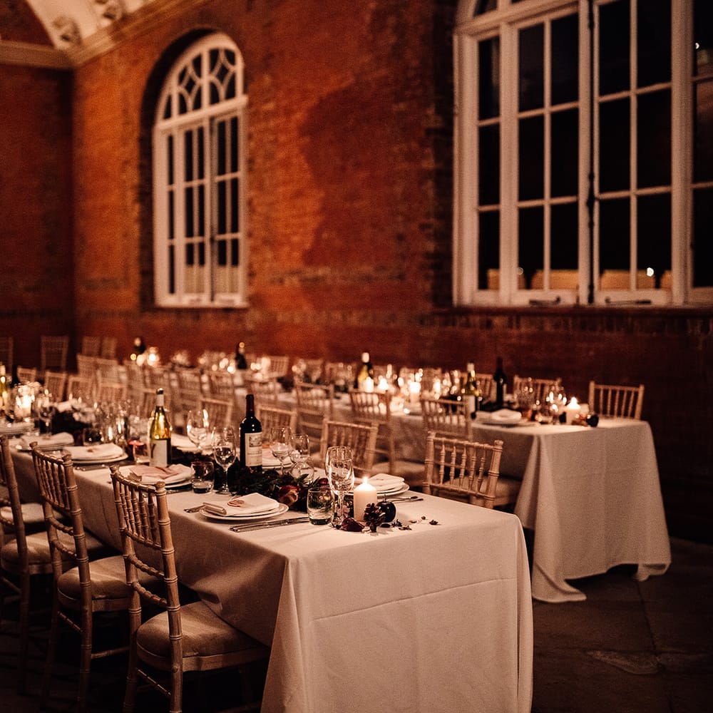 Long tables set with white table clothes, tall wine glasses with foilage and candles 