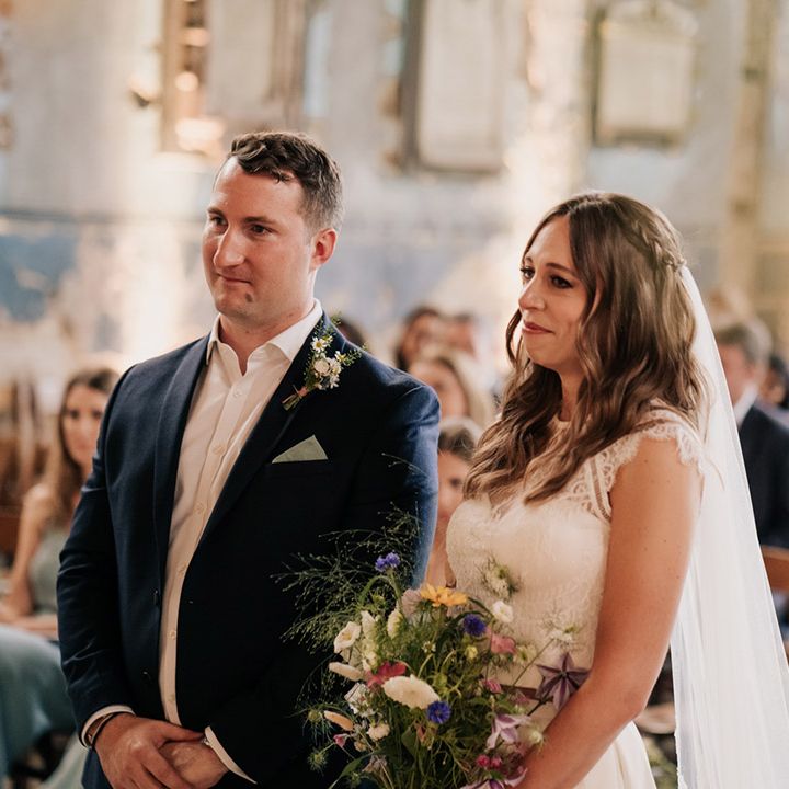 Bride in two piece wedding top and skirt and braided hairstyle and groom in navy blue suit jacket and wildflower boutonnière