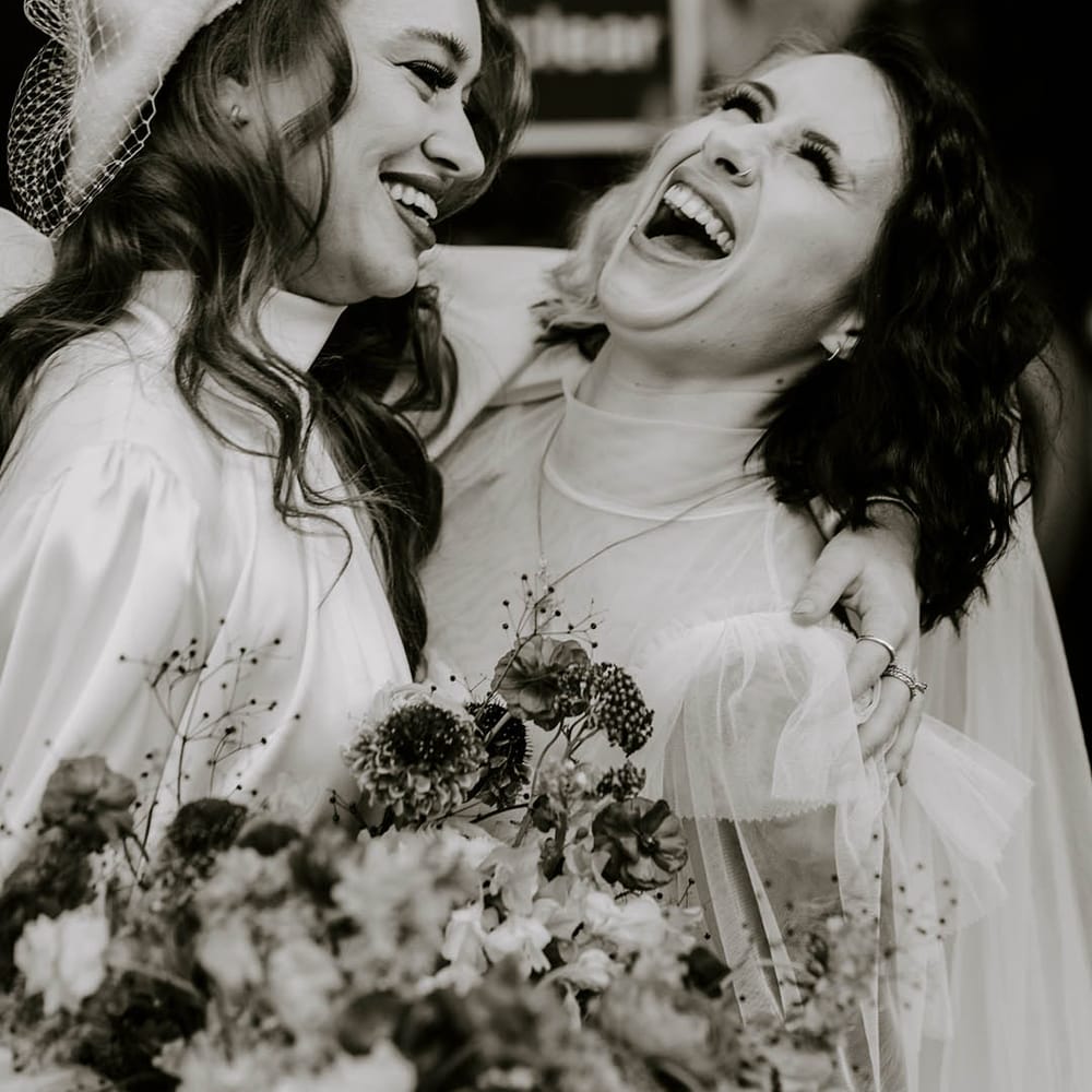 LGBTQI couple laughing in high neck wedding dresses 