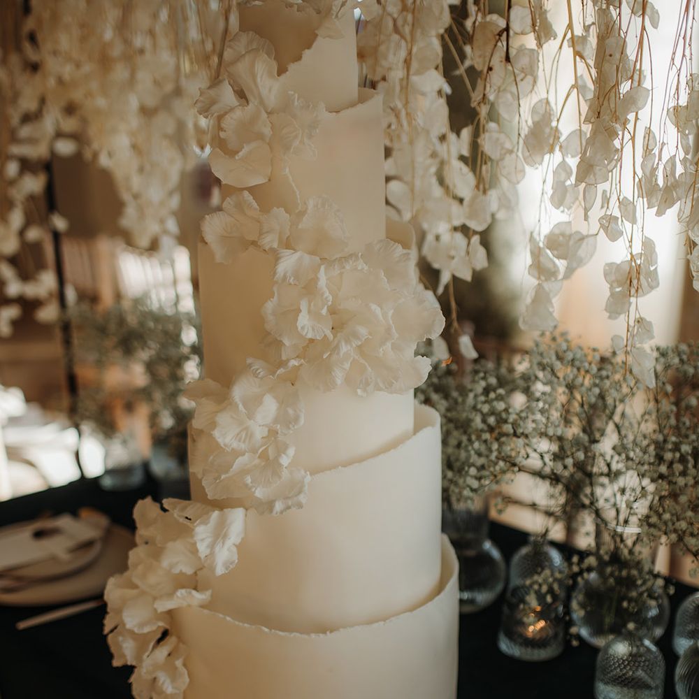 five tier buttercream wedding cake with ripple edge and cascading flower decor on the reception table 