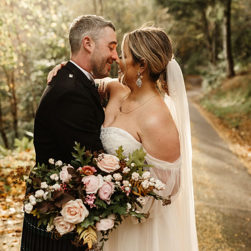 Bride and groom lean in for a kiss as they stand outside together on sunny autumn day 