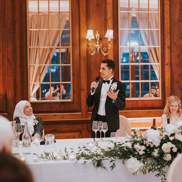 Groom in black tie stands reading out his speech