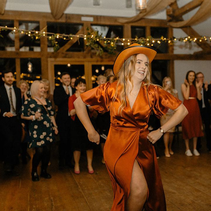 Wedding guest in burnt orange satin dress and matching cowboy hat dancing to music for weddings