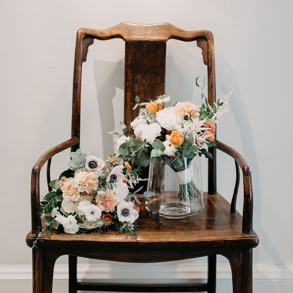 Wooden chair with bridal bouquets atop with white and orange blooms 