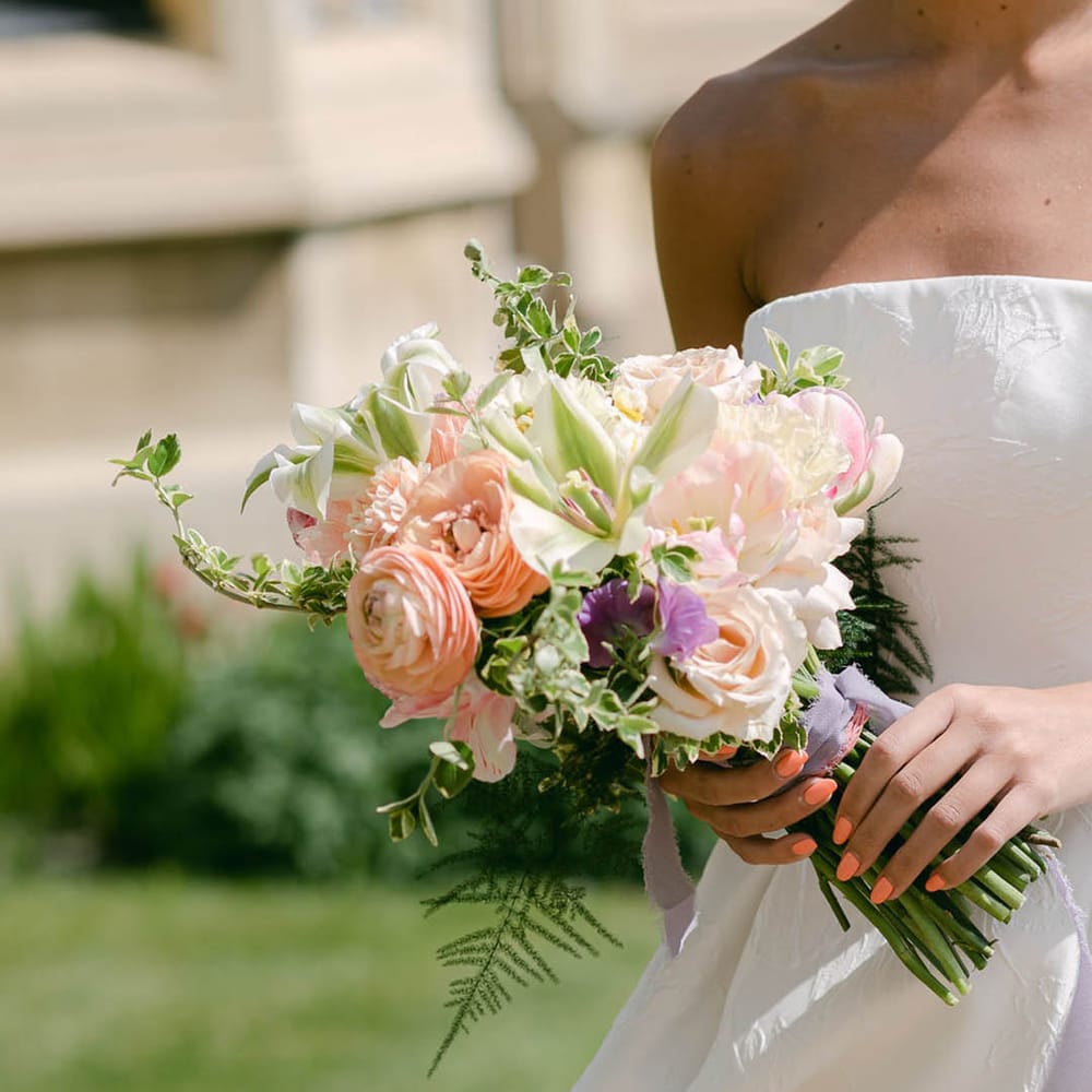 Bride with coral pink wedding nails holds a pastel wedding bouquet with roses and lilies 