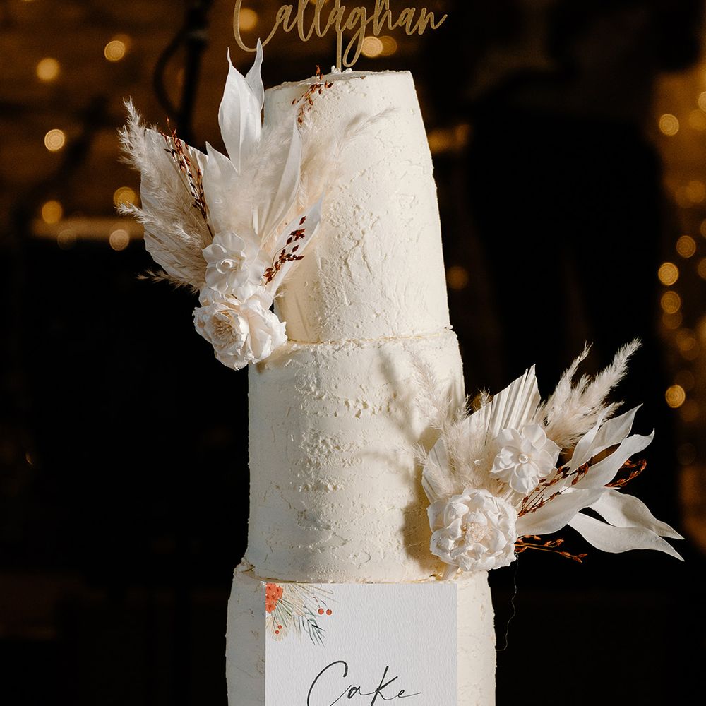 Three tier white iced wedding cake with pampas grass decoration and personalised wedding cake topper 