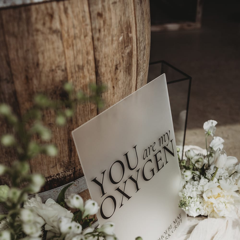 'You are my oxygen' frosted acrylic wedding sign leaning against a wooden barrel 