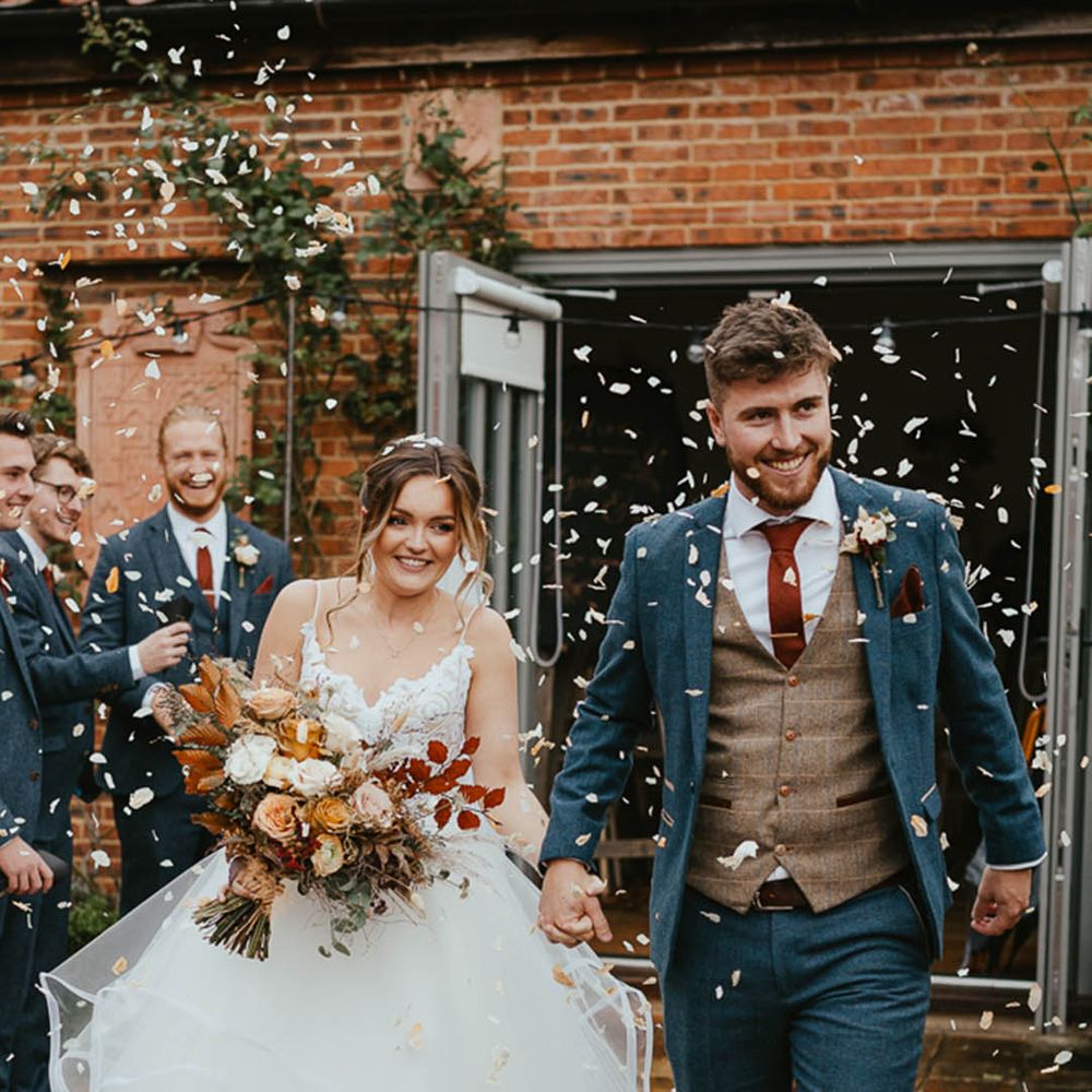 Bride in a princess wedding dress and the groom in a blue suit has a confetti exit form the ceremony 