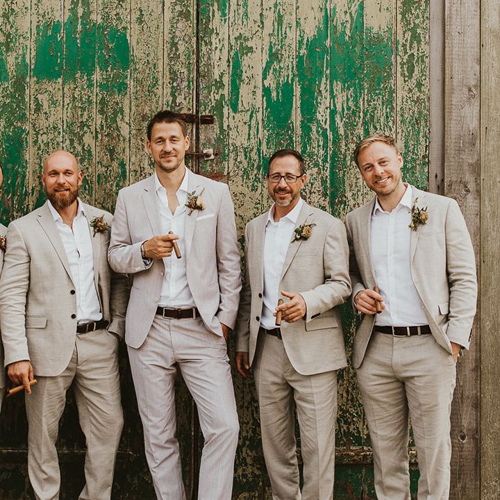 Groom standing with the groomsmen in matching light suits holding cigars 