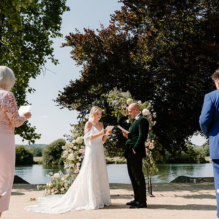 Bride & groom during outdoor wedding ceremony in front of floral archway 
