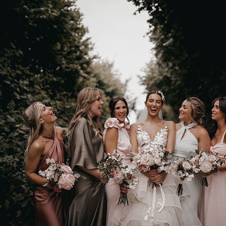 Bridesmaids in colourful mismatched dresses smile laughing with the bride 