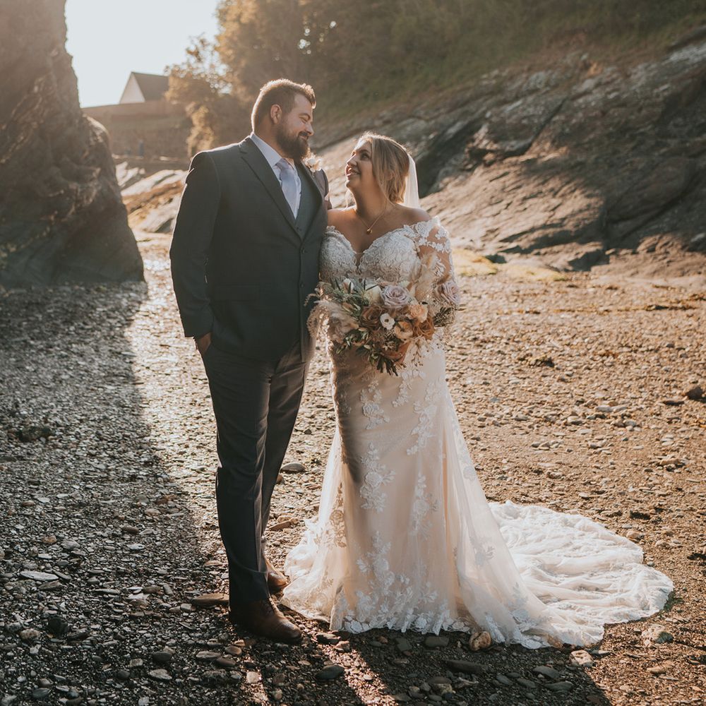 Bride & groom stand beside on another on the beach during golden hour on their wedding day 