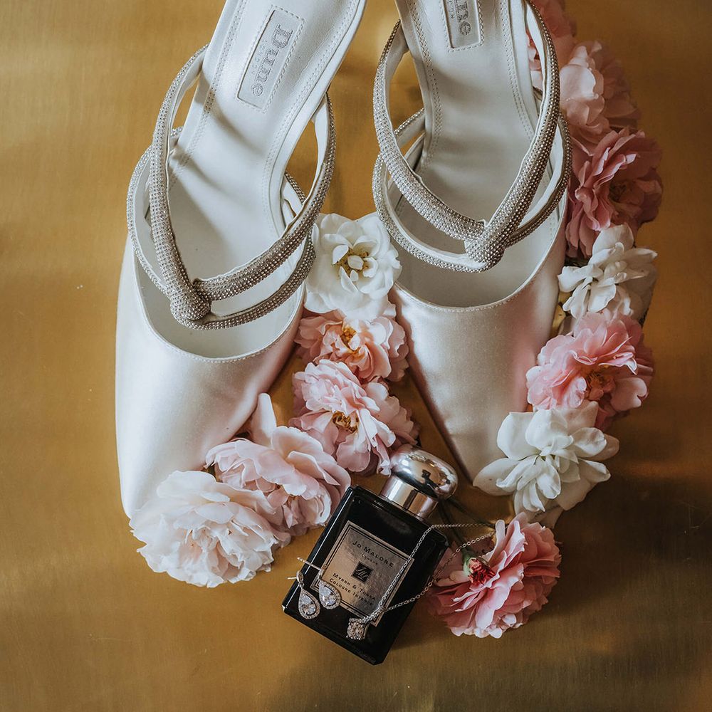 White satin pointed wedding shoes with the bride's Jo Malone perfume and silver jewellery 