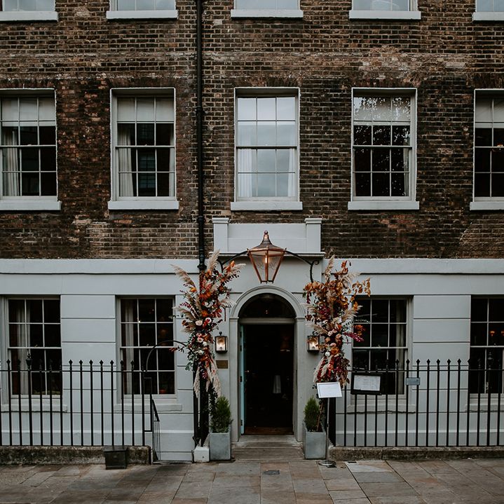 The Zetter Townhouse with large floral arch with roses, peonies, foliage and pampas grass in orange, red, yellow and green