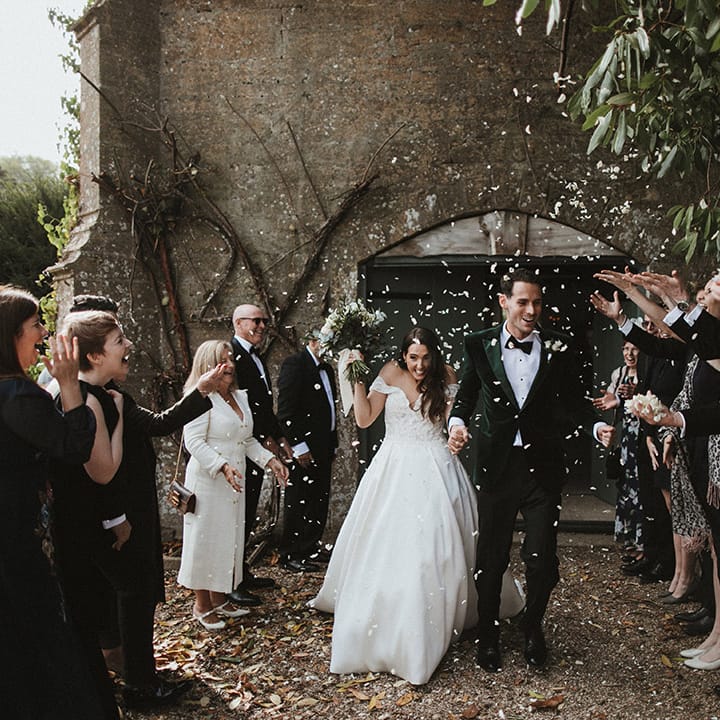 Classic and traditional wedding with the groom in a dark green tuxedo and bow tie align with the bride in luxe off the shoulder wedding dress to confetti 