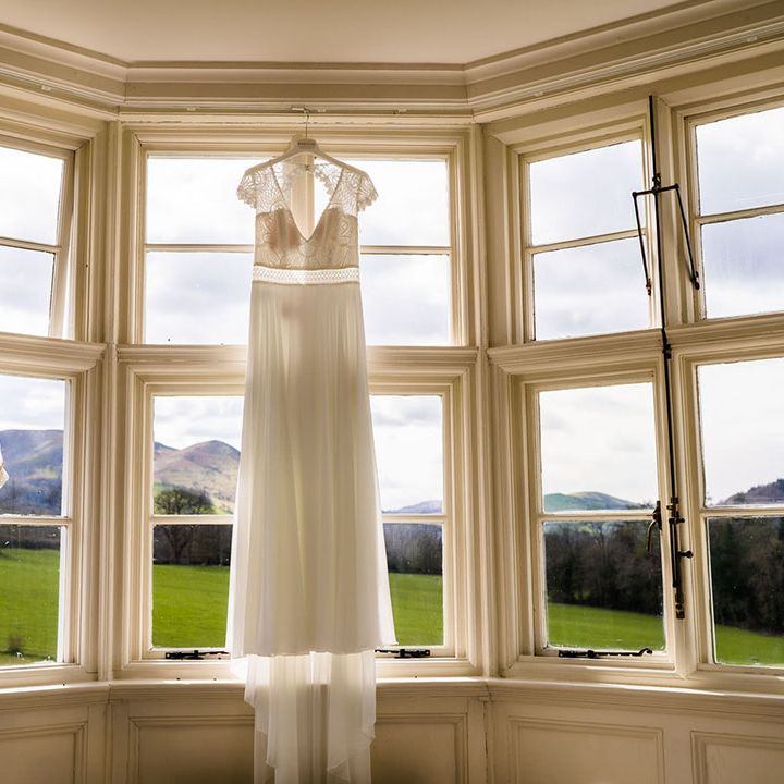 Lace wedding dress with capped sleeves hangs beside flower girl dress made from Mother Of The Bride's wedding dress
