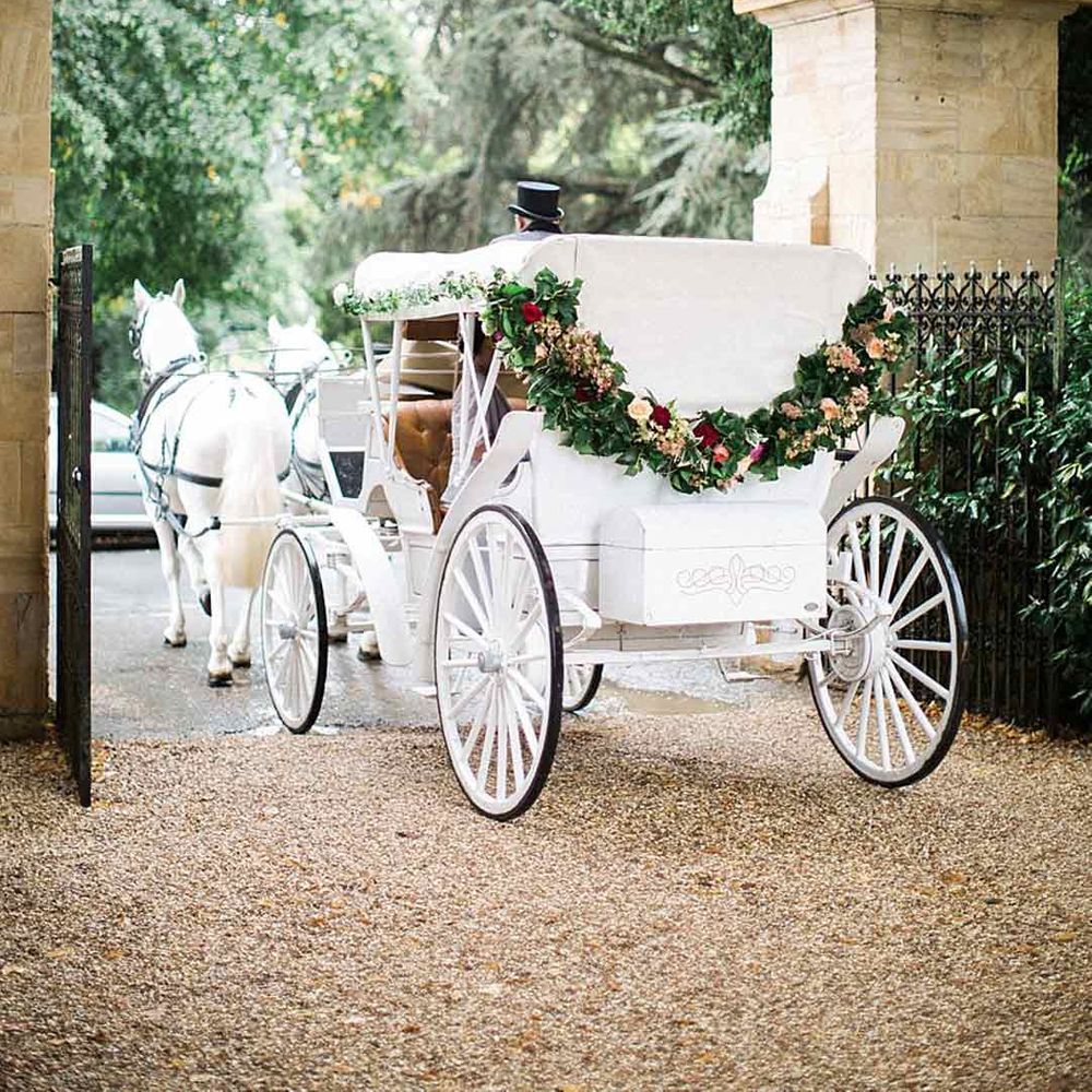White wedding horse-drawn carriage with floral wreath decorations - transport section of wedding budget spreadsheet 