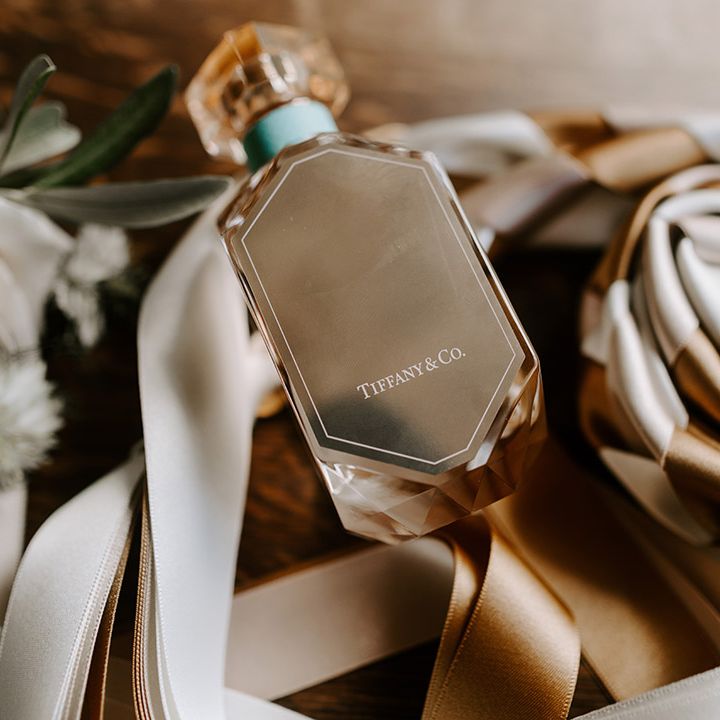 Gold Tiffany & Co. wedding perfume for the bride on satin cream and gold ribbons next to the bridal bouquet 