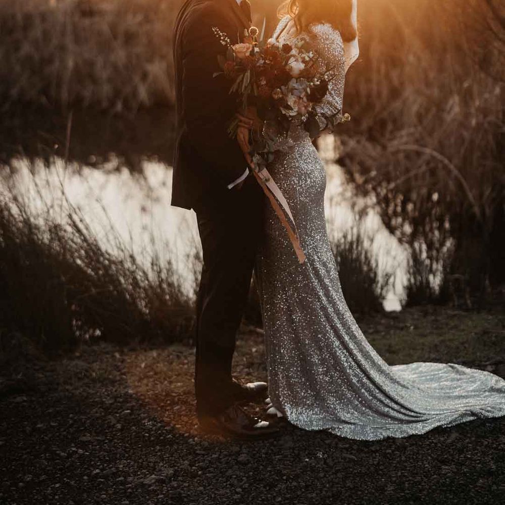 Bride in sparkly wedding dress and groom in classic black tuxedo doing couples golden hour photoshoot 