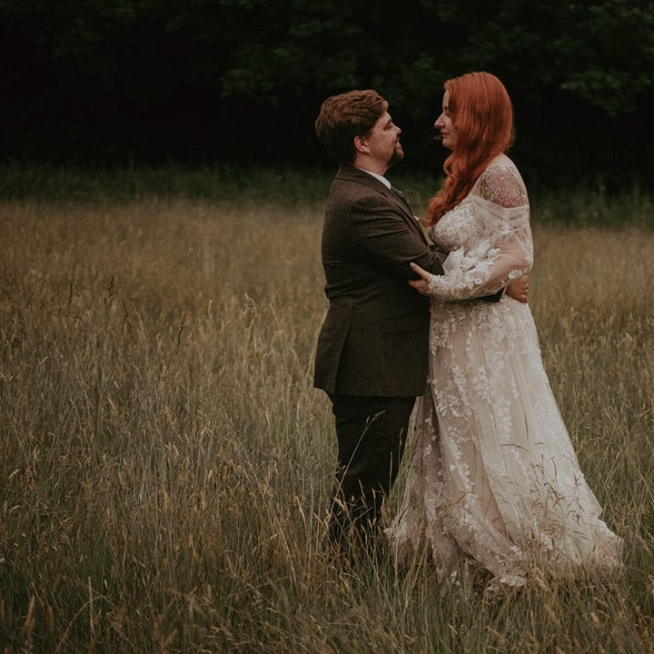 Groom in three piece suit embracing the bride in a boho off the shoulder long sleeve wedding dress with floral lace 