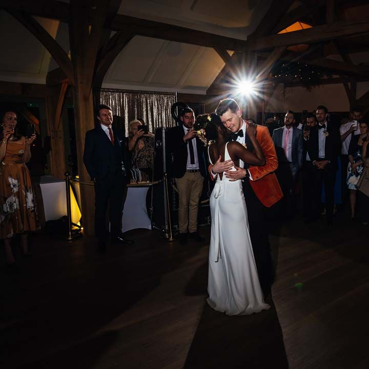 Bride in low back satin look wedding dress with 3D floral applique train slow dancing with groom in crushed burnt orange velvet grooms blazer, black bowtie and black suit trousers to their first dance wedding song