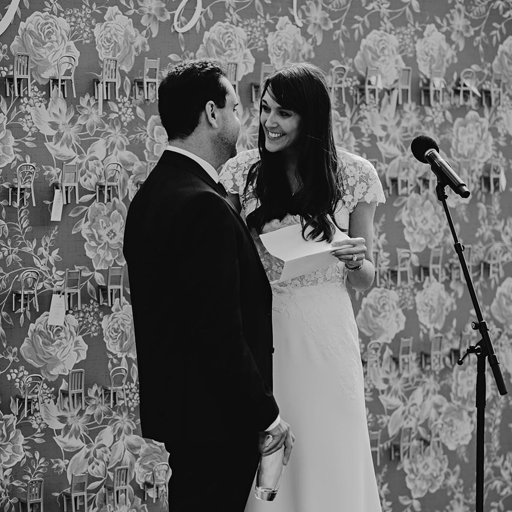 Bride in floral lace short sleeve wedding dress standing with the groom as they deliver their shared wedding speech 