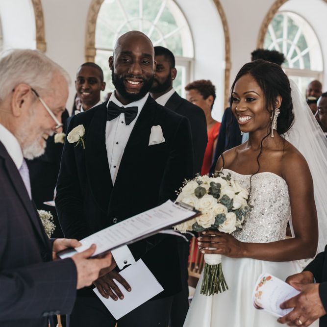 Black bride in a strapless Oleg Cassini wedding dress being given away at the altar by her father 