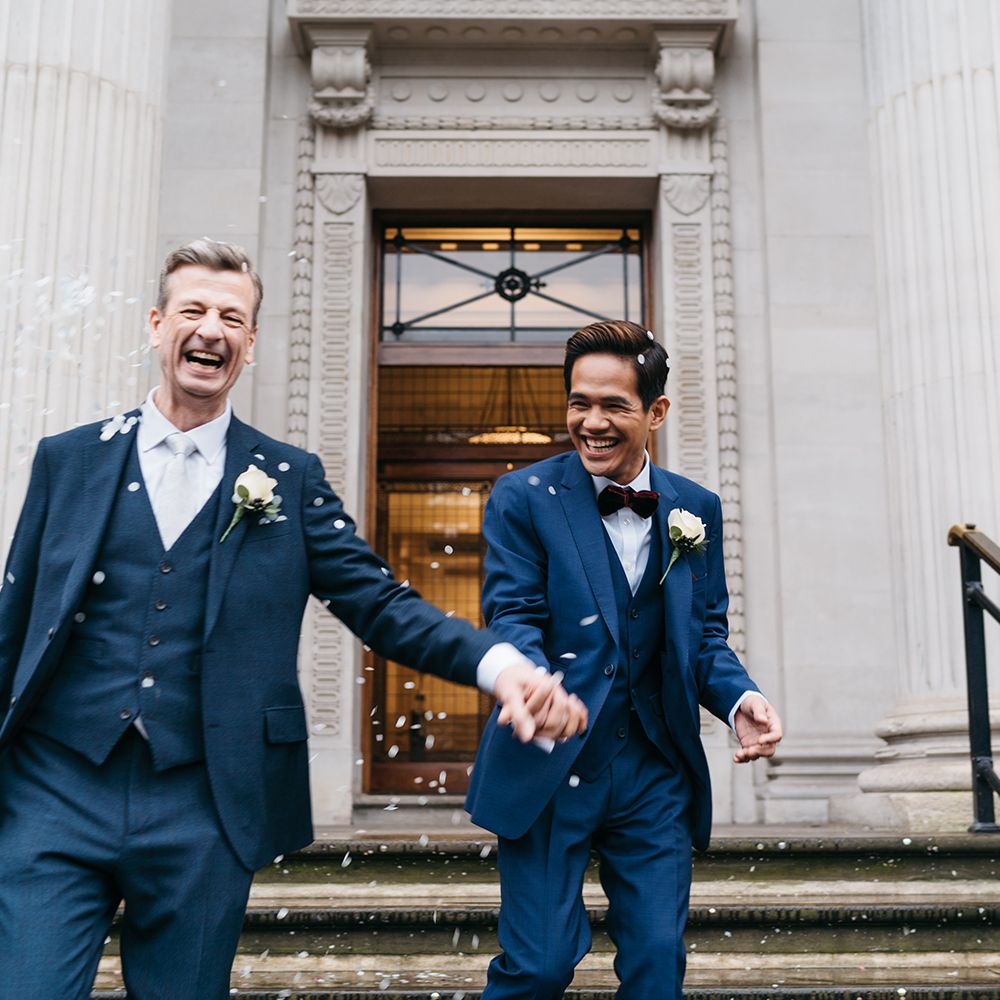 Grooms leave Old Marylebone Town Hall with confetti being thrown around them whilst holding hands