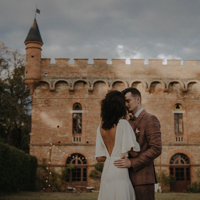 Bride and groom portrait in front of Château de Caumont with bride in a low V back wedding dress with button detail 