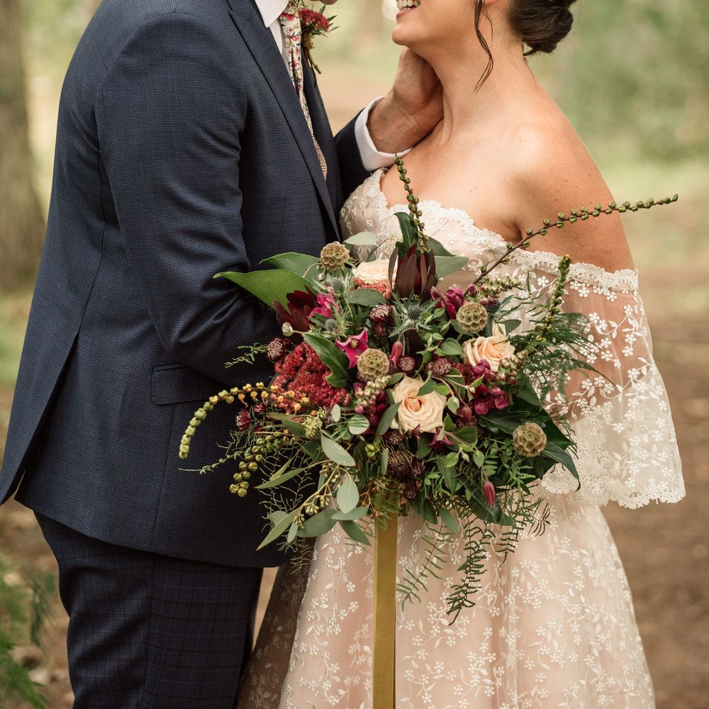Bride & groom lean in to kiss whilst bride holds floral bouquet