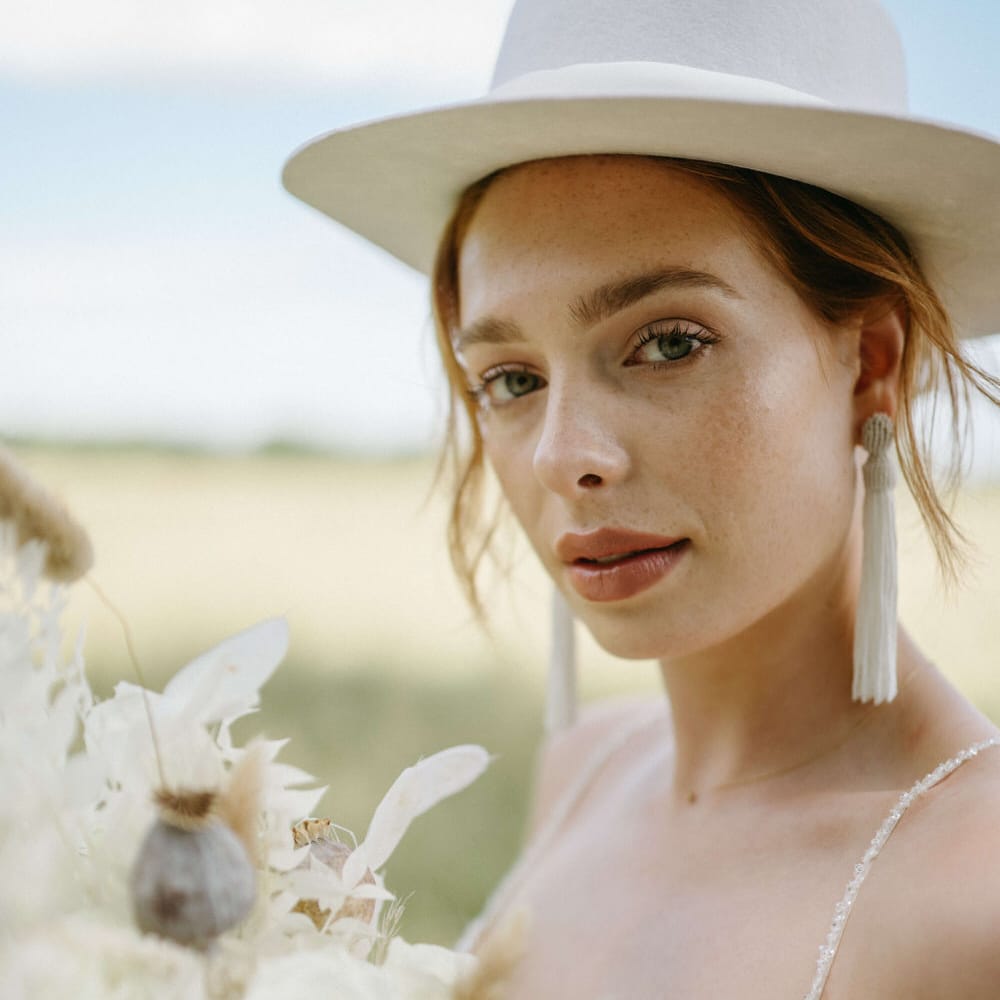 Bridal stetson hat, natural makeup, tassel earrings and an all white bouquet for boho wedding shoot at Berwick Lodge