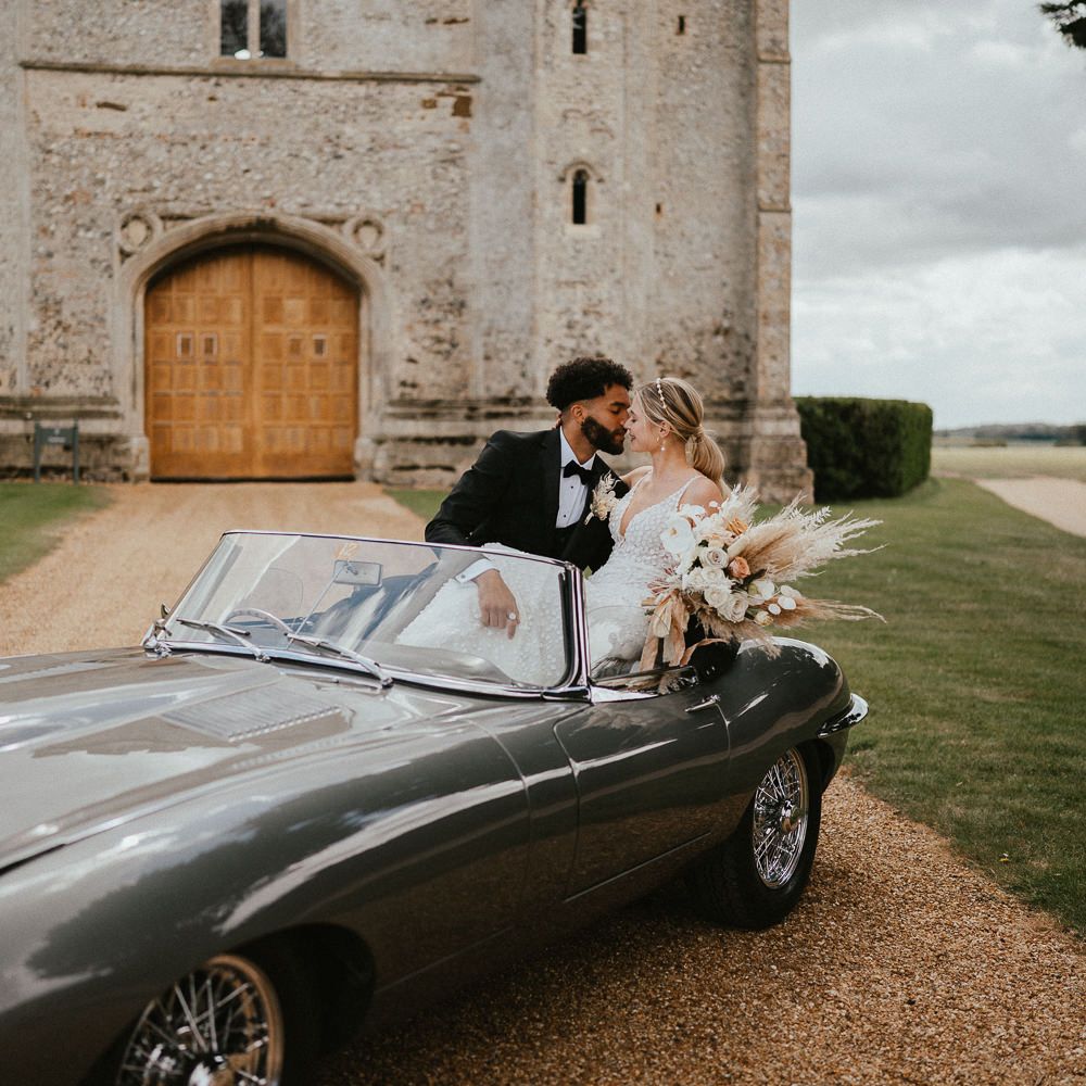 Bride and groom sitting in a classic convertible wedding car on the drive of Pentney Abbey